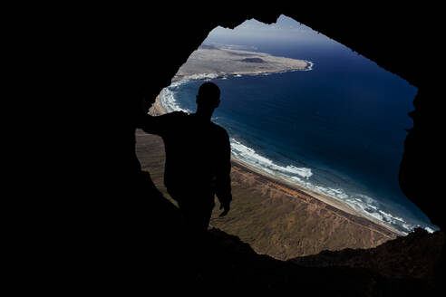 Silhouette eines Mannes aus einer Höhle auf der Famara-Klippe in Lanzarote, Spanien - CAVF80722