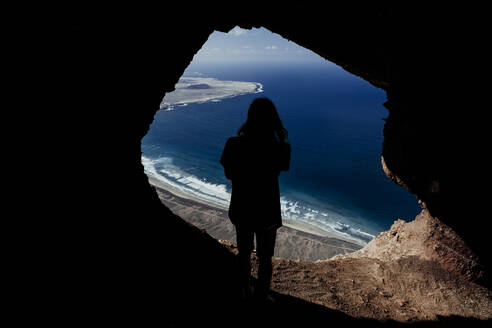 Silhouette eines Mannes aus einer Höhle in den Klippen von Famara auf Lanzarote - CAVF80724