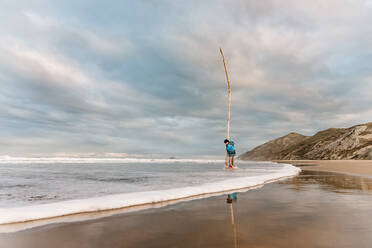 Tween carrying stick on beach in New Zealand - CAVF80730