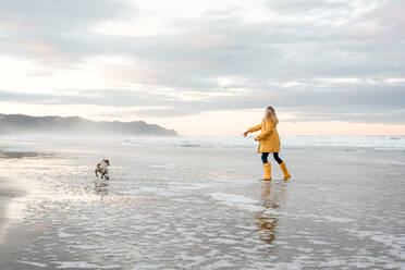 Mädchen im Teenageralter spielt mit Hund am Strand in Neuseeland - CAVF80733