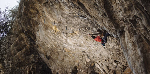 Climber sending a hard sport climbing route in a cave. - CAVF80822