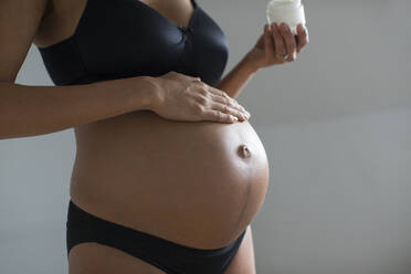 Close up pregnant woman applying moisturizer to stomach - HOXF06230