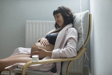 Gelassene schwangere Frau, die sich den Bauch reibt - HOXF06234