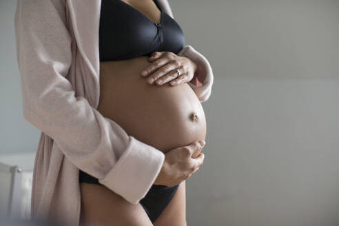 Schwangere Frau in BH und Höschen hält Bauch - HOXF06244