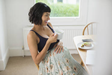 Happy pregnant woman drinking tea at laptop - HOXF06248