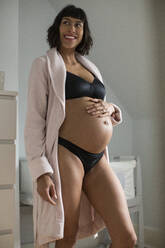Glückliche schwangere Frau in BH und Höschen hält Bauch - HOXF06249