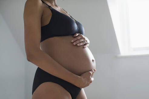Schwangere Frau in BH und Höschen hält Bauch - HOXF06253