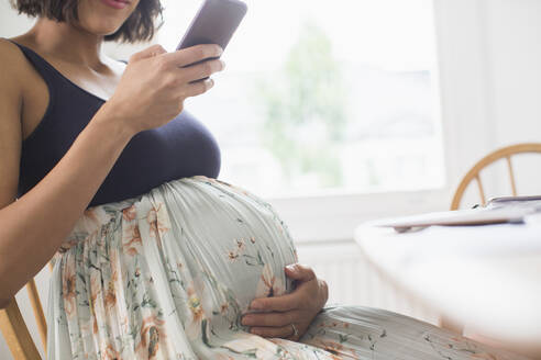 Schwangere Frau in geblümtem Kleid mit Smartphone - HOXF06254