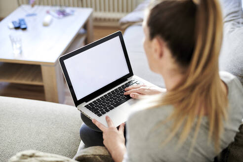 Hohe Winkelansicht der Frau, die einen Laptop benutzt, während sie zu Hause auf dem Sofa sitzt - MMIF00239