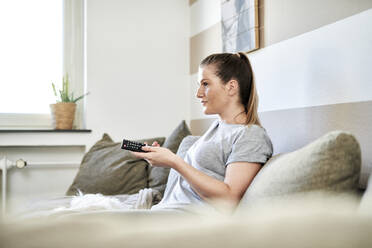 Frau sieht fern, während sie zu Hause auf dem Sofa sitzt - MMIF00242