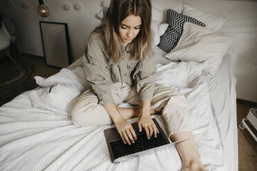 Hohe Winkel Ansicht der Frau mit Laptop, während auf dem Bett zu Hause sitzen - LHPF01274