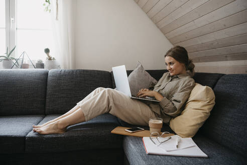 Frau benutzt Laptop, während sie zu Hause auf dem Sofa sitzt - LHPF01286