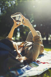 Young woman relaxing and using digital tablet in sunny summer park - CAIF26297