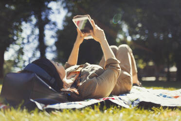 Junge Frau benutzt digitales Tablet in einem sonnigen Sommerpark - CAIF26299