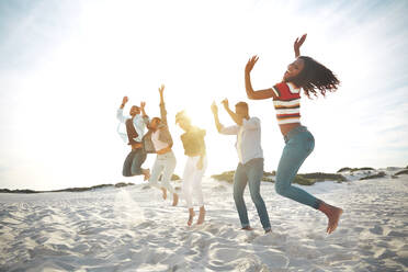 Portrait playful, energetic young friends jumping for joy on sunny summer beach - CAIF26302