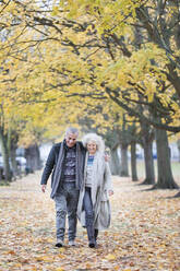 Zärtliches älteres Paar, das zwischen Bäumen und Blättern im Herbstpark spazieren geht - CAIF26376