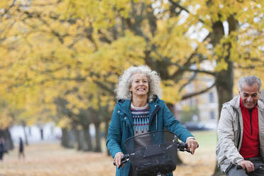 Lächelnde, unbekümmerte ältere Frau auf dem Fahrrad zwischen Bäumen im Herbstpark - CAIF26380