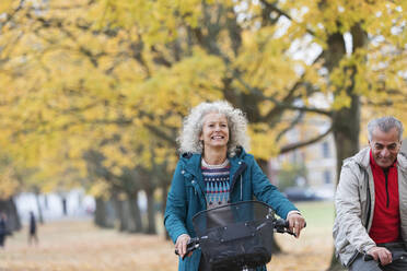 Smiling, carefree senior woman bike riding among trees in autumn park - CAIF26380