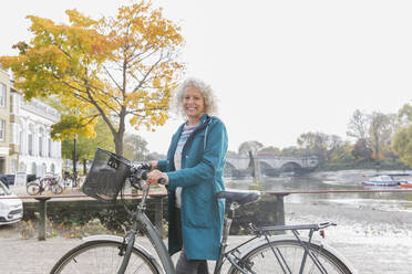 Porträt lächelnd ältere Frau Fahrradfahren entlang Herbst Fluss - CAIF26381