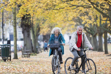 Älteres Paar fährt mit dem Fahrrad zwischen Bäumen und Blättern im Herbstpark - CAIF26382