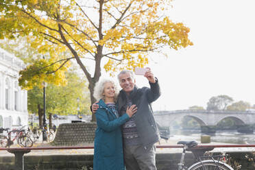 Senior couple taking selfie in front of autumn tree - CAIF26386