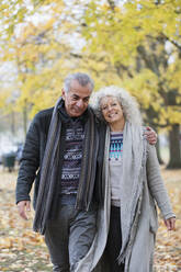 Selbstbewusstes, lächelndes älteres Paar, das sich umarmt und im Herbstpark spazieren geht - CAIF26387