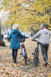 Älteres Paar, das zwischen Bäumen und Blättern im Herbstpark Fahrrad fährt - CAIF26390