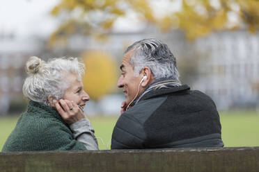 Glückliches älteres Paar mit Kopfhörern, das im Park Musik hört - CAIF26397