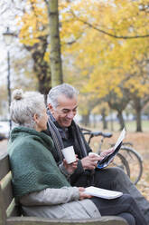 Älteres Paar liest Zeitung und trinkt Kaffee auf einer Bank im Herbstpark - CAIF26402