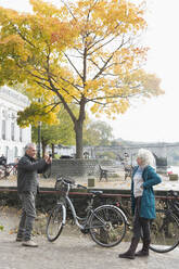 Älterer Mann fotografiert Frau mit Fahrrad in herbstlicher Stadt - CAIF26406