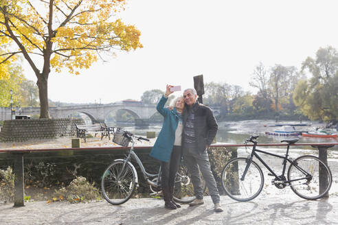 Älteres Paar mit Fahrrädern macht Selfie am herbstlichen Fluss - CAIF26411