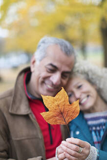 Zärtliches älteres Paar hält orangefarbenes Herbstblatt - CAIF26415