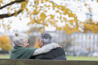 Unbeschwertes, zärtliches älteres Paar, das sich auf einer Bank im Herbstpark umarmt - CAIF26416