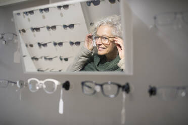 Senior woman trying on eyeglasses in optometry shop - CAIF26436