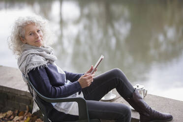 Porträt einer selbstbewussten, aktiven älteren Frau, die ein digitales Tablet am Parkteich benutzt - CAIF26440