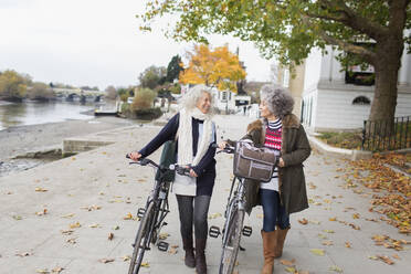 Smiling active senior women walking bicycles in autumn park - CAIF26442