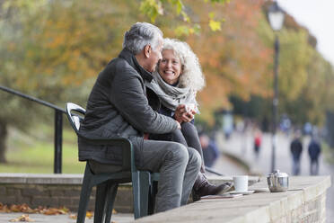 Smiling, affectionate active senior couple drinking tea in autumn park - CAIF26446