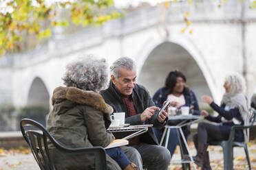 Aktives älteres Ehepaar, das ein Smartphone benutzt und Kaffee im Herbstparkcafé trinkt - CAIF26454