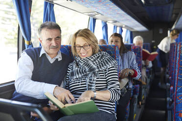 Aktives älteres Touristenpaar liest ein Buch im Reisebus - CAIF26464