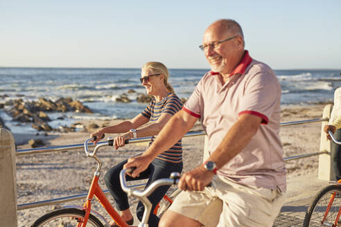 Lächelnde aktive Seniorentouristen beim Radfahren am sonnigen Meer - CAIF26474