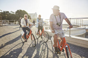 Active senior tourist friends bike riding on sunny boardwalk - CAIF26482