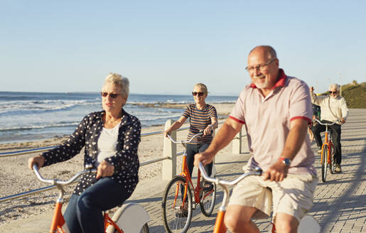 Aktive ältere Touristenfreunde beim Radfahren auf der sonnigen Strandpromenade am Meer - CAIF26488