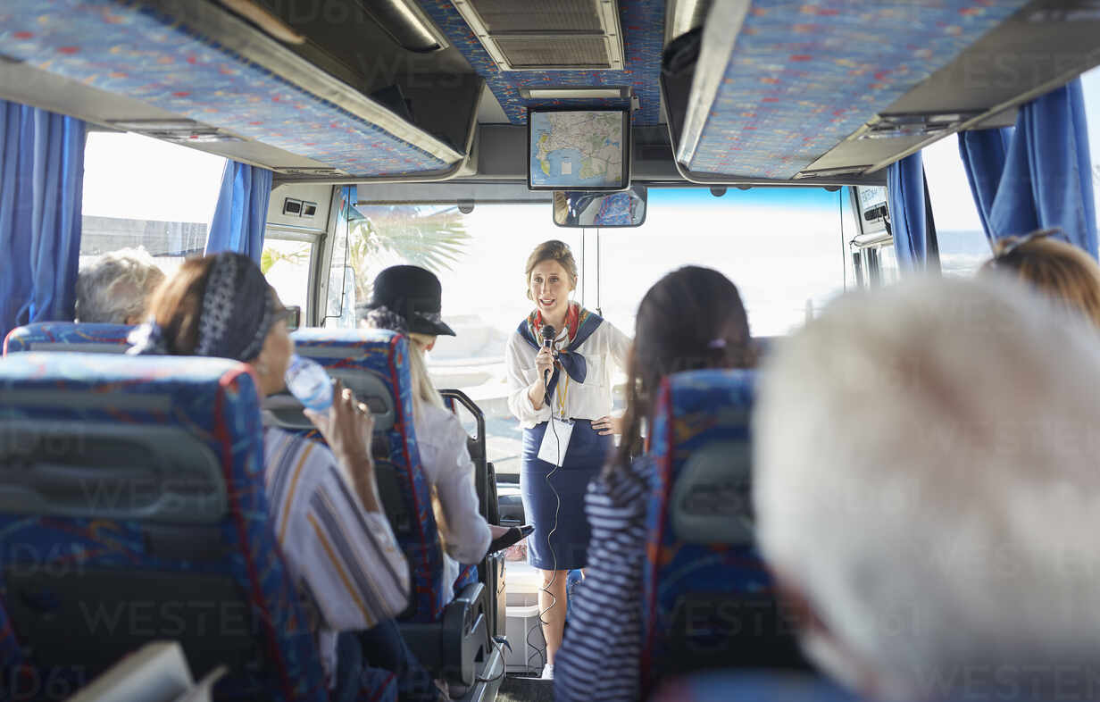 Female Tour Guide With Microphone Talking To Active Senior Tourists On Tour Bus CAIF26498 