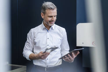 Lächelnder Geschäftsmann mit Werkstück und Tablet in einer Fabrik - DIGF10094