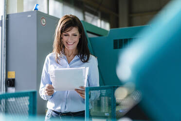 Smiling businesswoman reviewing papers in a factory - DIGF10125