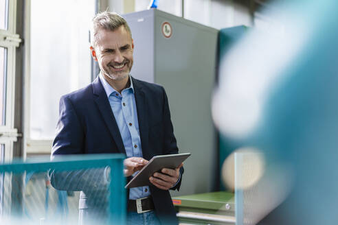 Lächelnder Geschäftsmann, der ein Tablet in einer Fabrik benutzt - DIGF10127