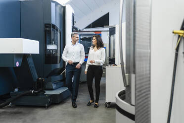 Businessman and businesswoman walking and talking in a factory - DIGF10157