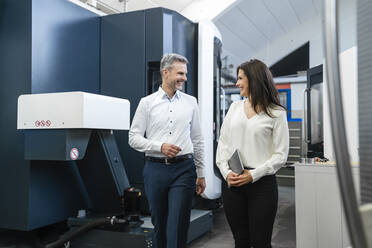 Happy businessman and businesswoman walking in a factory - DIGF10160