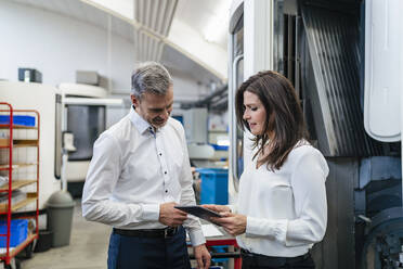 Businessman and businesswoman with tablet having a work meeting in a factory - DIGF10164