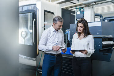 Businessman and businesswoman with product and tablet having a work meeting in a factory - DIGF10179